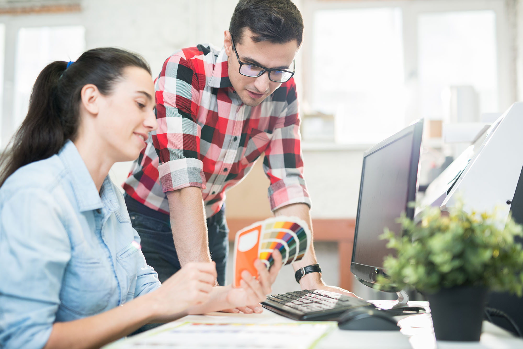 One female and male office worker looking through color samples while in front of computer