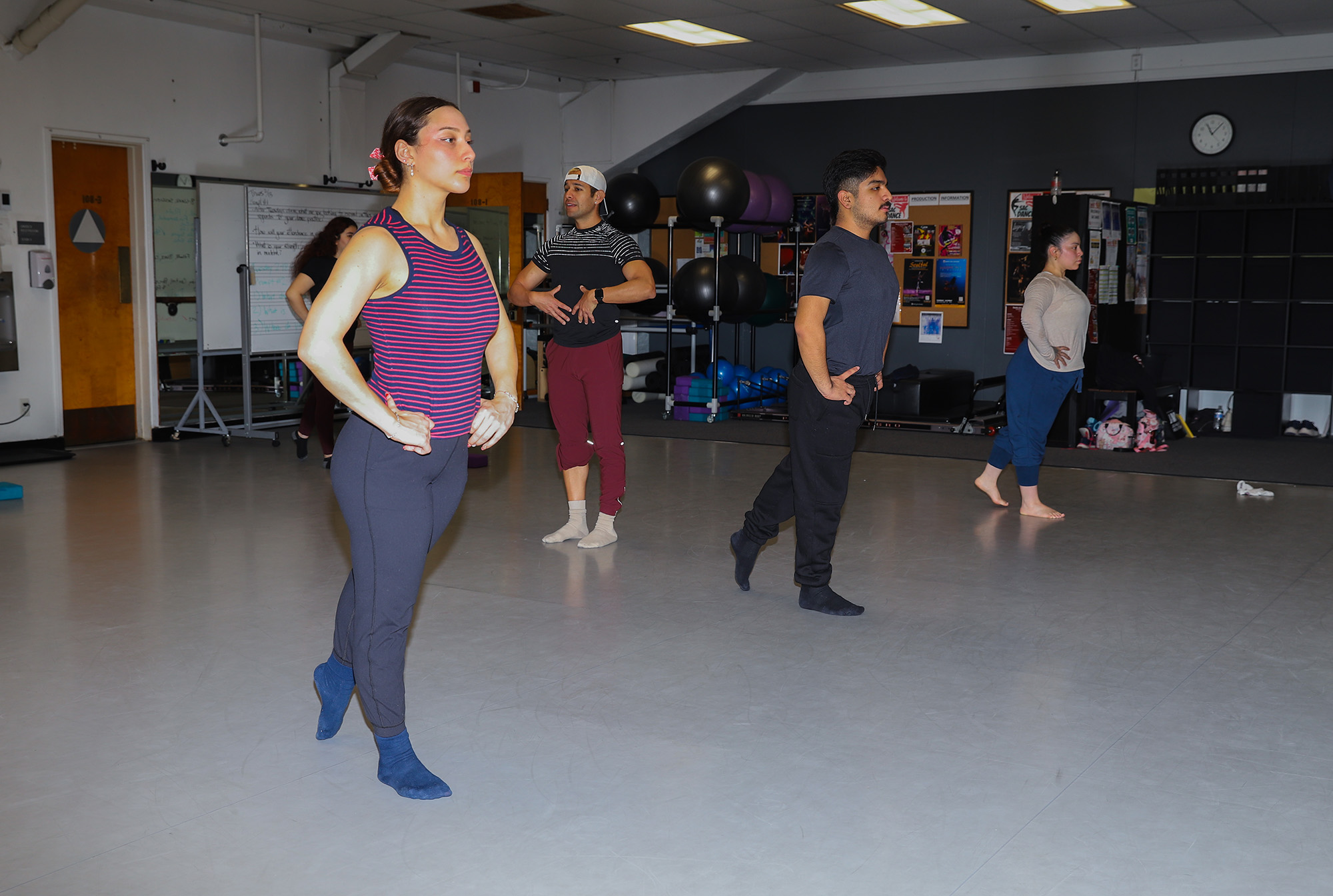 two female and one male dance student standing in line on tippy toes at a dance studio