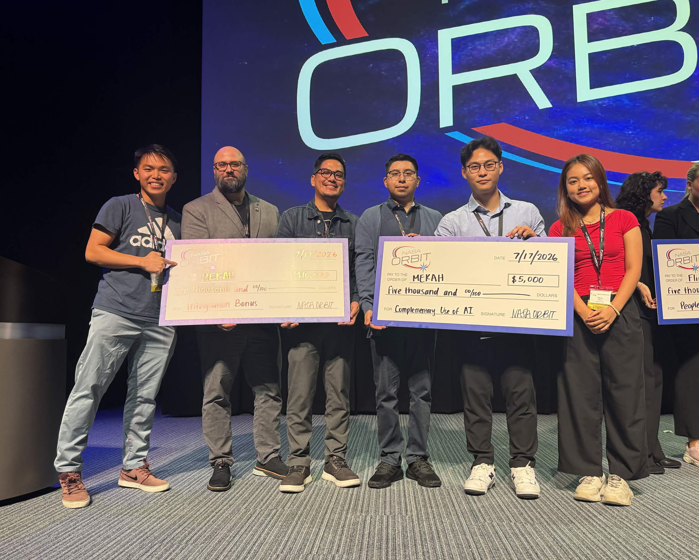 Team MEKAH students and Dr. Alex Natale pose with two giant checks