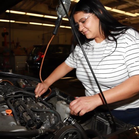 Latina woman working on car in automotive technology class with Santa Ana School of Continuing Education