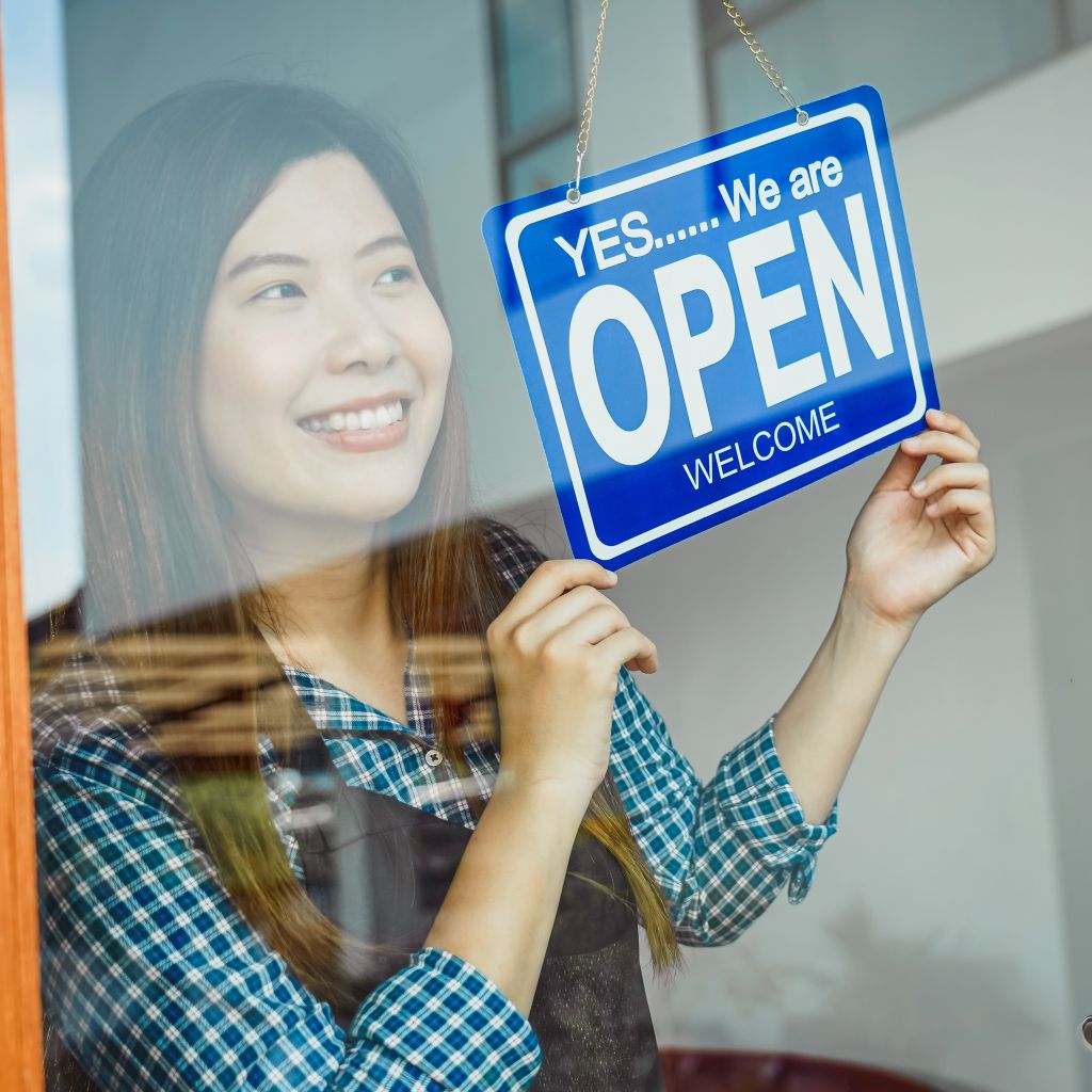 Woman holding OPEN sign in front of store