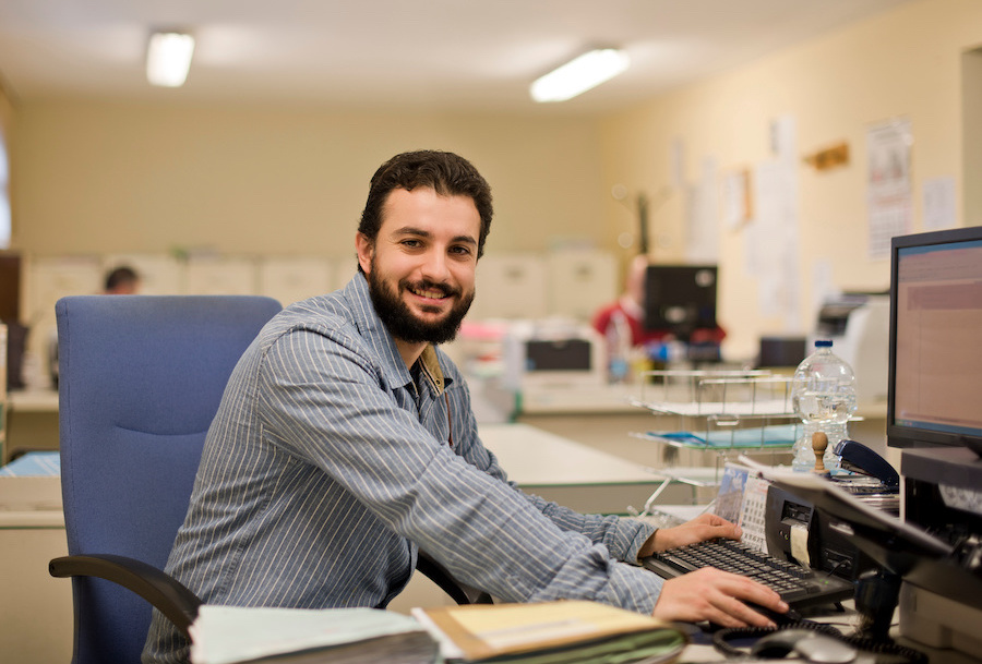 Bearded male employee smiling while working at a computer in an office after getting certificates from Santa Ana College