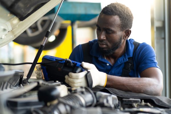 African American man repairing car, using skills learned from free automotive technology classes at continuing education