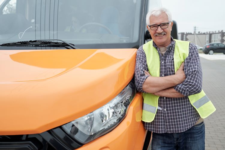 Older male bus operator standing outside of bus smiling because of career with OCTA